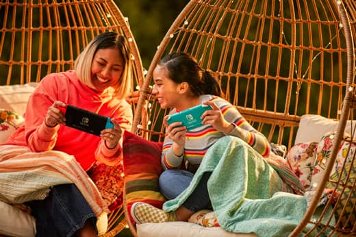 A woman and young girl are playing on a Nintendo Switch system outside.